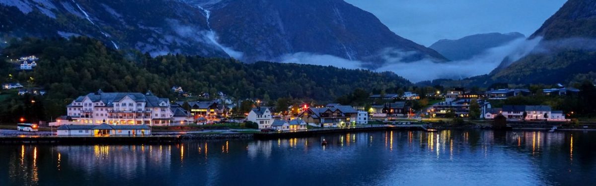 A view of a city in Norway from the water, with mountains in the background.