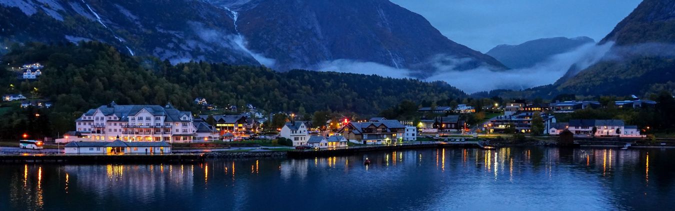 A view of a city in Norway from the water, with mountains in the background.